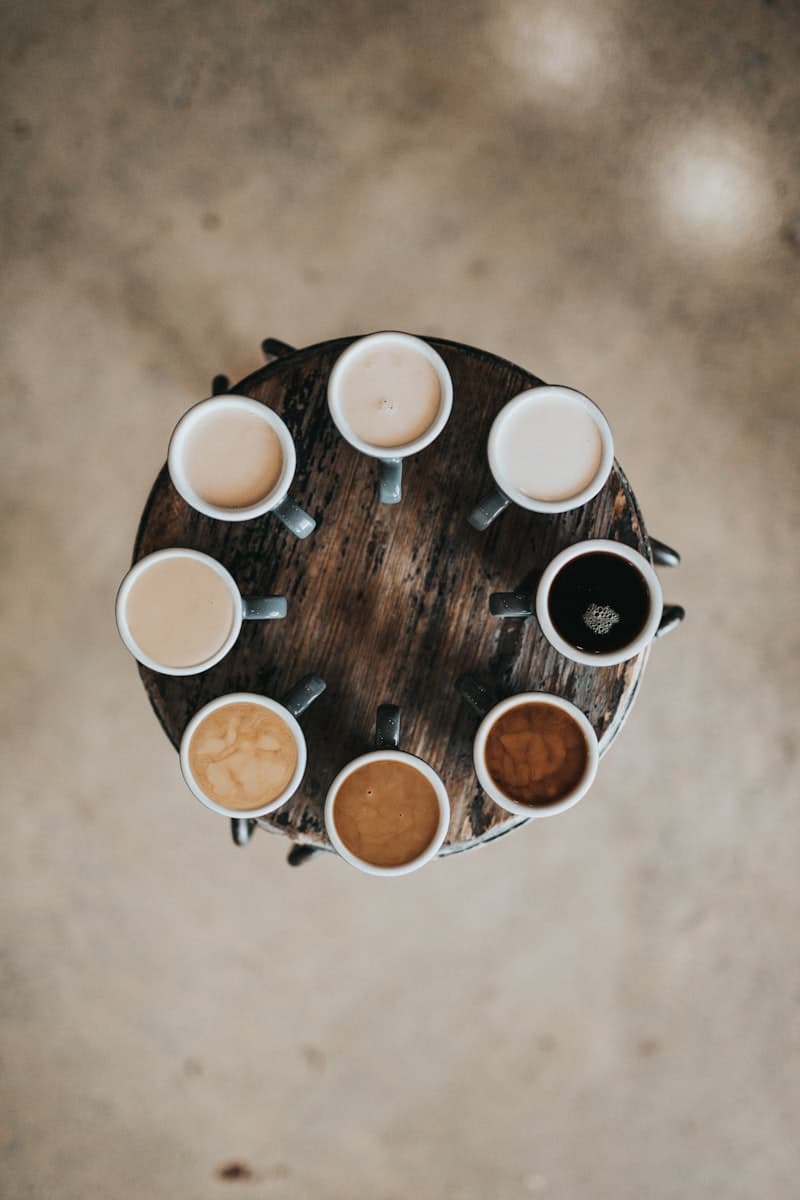 A round wooden table set with multiple cups of coffee viewed from above.